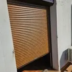 Volet roulant aluminium couleur bois en position semi-fermée installé sur une baie vitrée, avec coffre extérieur et coulisses latérales, off