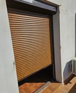 Volet roulant aluminium couleur bois en position semi-fermée installé sur une baie vitrée, avec coffre extérieur et coulisses latérales, off