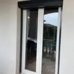 Fenêtre double avec menuiserie blanche équipée d’un volet roulant aluminium gris anthracite avec coffre extérieur, installé pour amélior